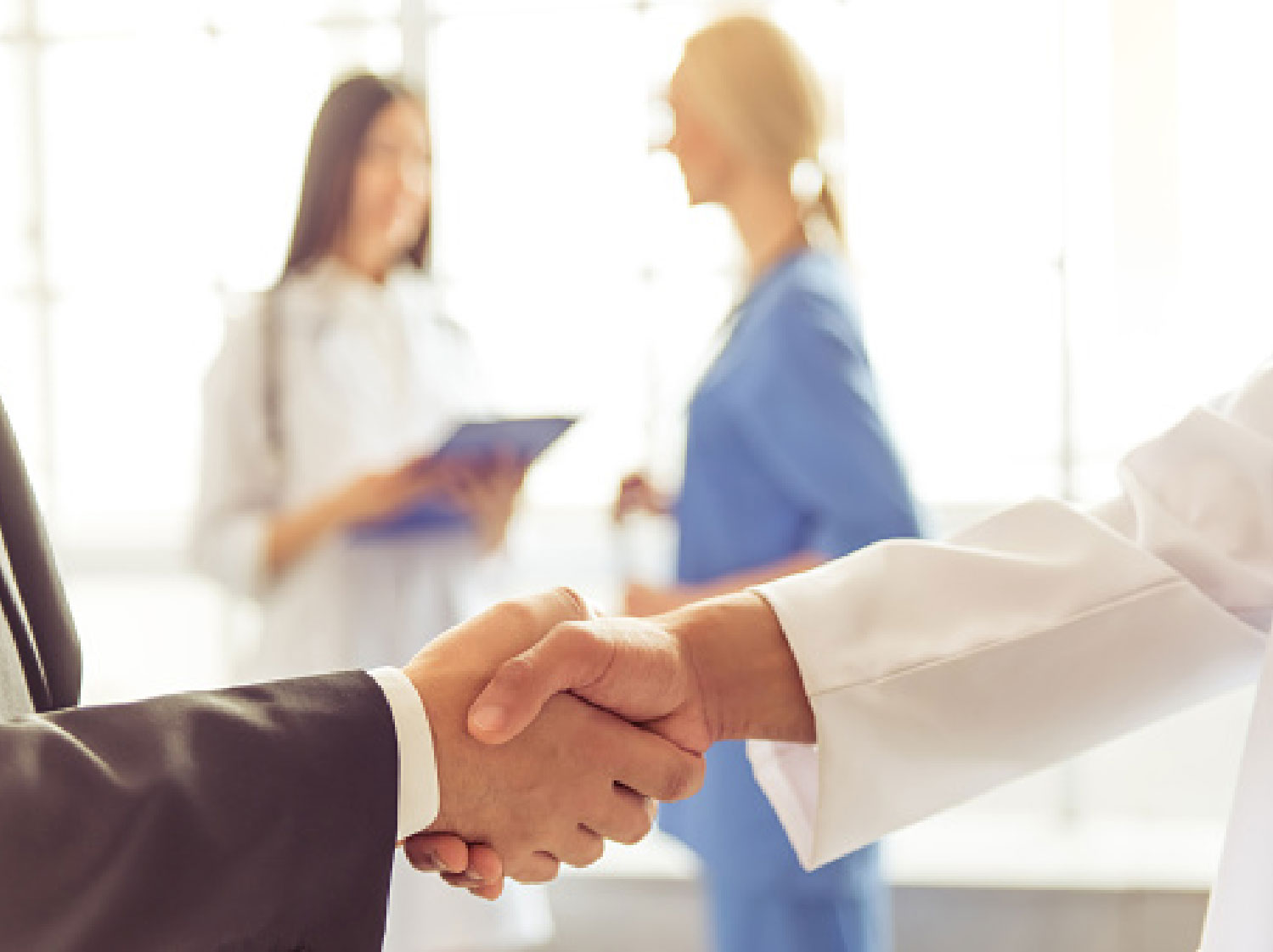 HCI-why-we-do-it-home 2 people shaking hands with doctor and nurse in background